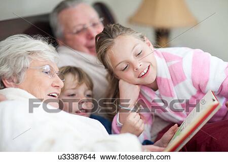 Grandparents and grandchildren reading storybook in bed View Large Photo Image Picture - Grandparents and grandchildren reading storybook in bed. Fotosearch