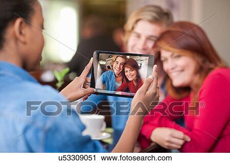 Stock Image - Group of friends in cafe taking photograph with digital tablet. Fotosearch