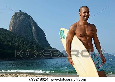 Man carrying surfboard on beach, Rio de Janeiro, Brazil View Large Photo Image Picture - Man carrying surfboard on beach, Rio de Janeiro, Brazil. Fotosearch