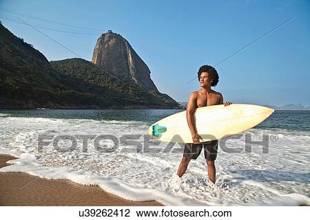 Man holding surfboard on beach, Rio de Janeiro, Brazil View Large Photo Image Stock Image - Man holding surfboard on beach, Rio de Janeiro, Brazil. Fotosearch