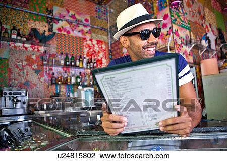 Stock Image - Man in hat and sunglasses, holding menu. Fotosearch