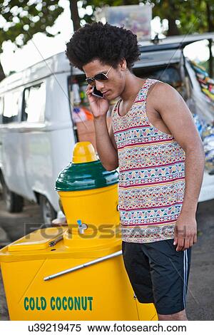 Stock Photography - Man on cell phone with cold coconut drinks stall. Fotosearch