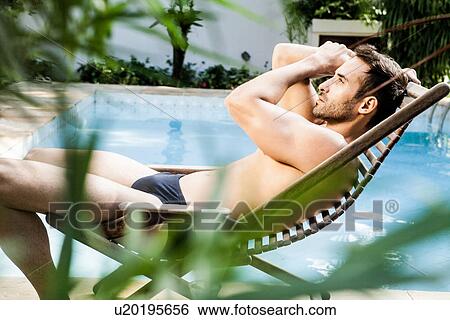 Stock Photograph - Man reclining on sunlounger by swimming pool. Fotosearch