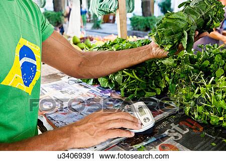Stock Image - Man using calculator on market stall. Fotosearch