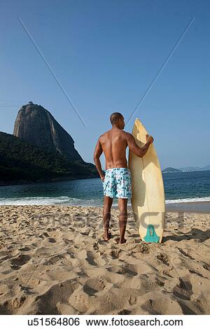 Stock Photograph - Man with surfboard on beach, Rio de Janeiro, Brazil. Fotosearch