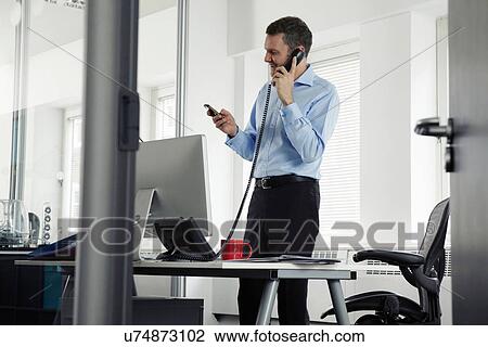 Stock Image - Mature businessman on landline phone in office. Fotosearch