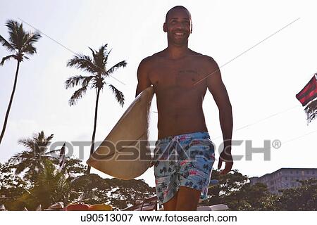 Stock Photo - Mid adult man carrying surfboard. Fotosearch