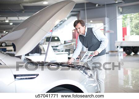 Mid adult man checking car bonnet in showroom View Large Photo Image Stock Image - Mid adult man checking car bonnet in showroom. Fotosearch