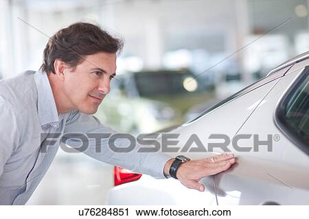 Mid adult man examining car in showroom View Large Photo Image Stock Image - Mid adult man examining car in showroom. Fotosearch