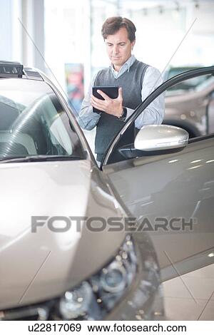 Mid adult man using calculator in car showroom View Large Photo Image Stock Photo - Mid adult man using calculator in car showroom. Fotosearch