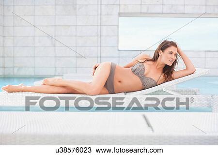 Stock Image - Mid adult woman in bikini lying on pool sunbed. Fotosearch