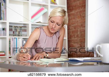Mid adult woman making notes at desk View Large Photo Image Stock Photo - Mid adult woman making notes at desk. Fotosearch