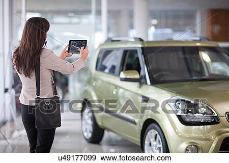 Mid adult woman taking photograph of car in showroom View Large Photo Image Stock Photo - Mid adult woman taking photograph of car in showroom. Fotosearch
