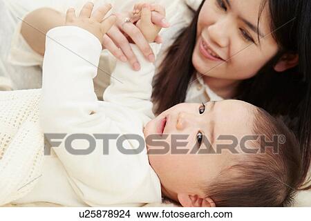 Picture - Mother and baby boy lying together holding hands. Fotosearch