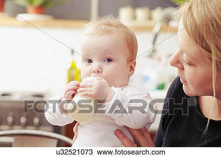 Stock Image - Mother and baby sitting in kitchen with baby bottle. Fotosearch