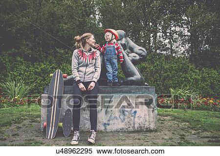 Stock Photography - Mother and daughter resting on park plinth with skateboards. Fotosearch