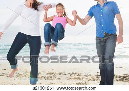 Stock Image - Mother and parents swinging girl on beach. Fotosearch