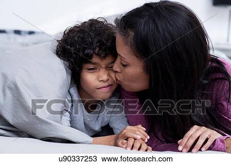 Stock Image - Mother kissing son on cheek in bed. Fotosearch