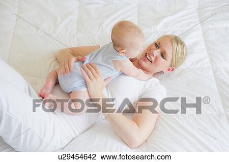 Stock Image - Mother lying on bed hugging baby. Fotosearch