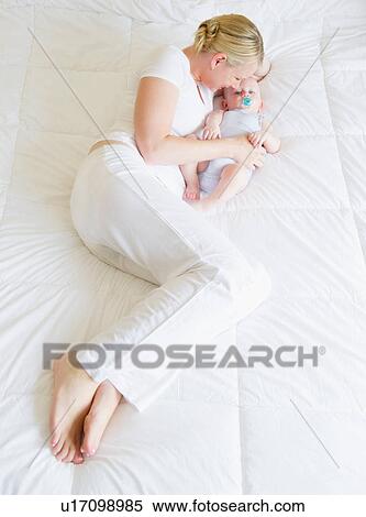 Stock Photography - Mother lying on bed hugging baby. Fotosearch