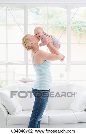 Stock Image - Mother standing holding baby, kissing cheek. Fotosearch