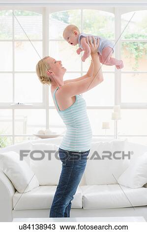 Stock Image - Mother standing holding up baby. Fotosearch