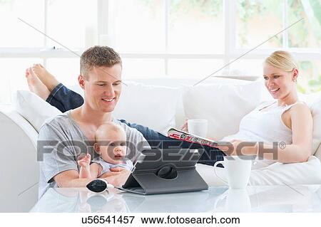 Stock Photo - Parents sitting with baby looking at digital tablet. Fotosearch