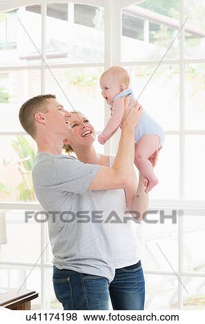 Stock Photo - Parents standing holding up baby. Fotosearch