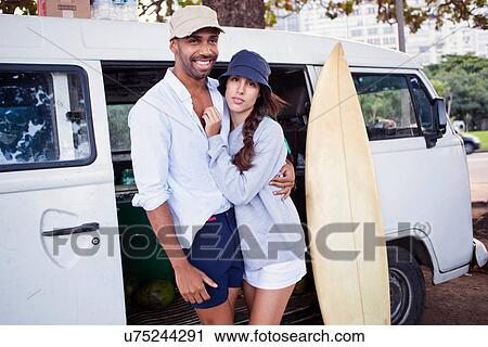 Stock Image - Portrait of couple by campervan with surfboard. Fotosearch