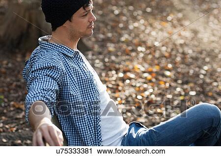 Stock Image - Portrait of man sitting on bench in autumn. Fotosearch