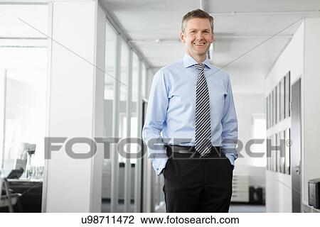 Stock Image - Portrait of mature businessman in office, hands in pockets. Fotosearch