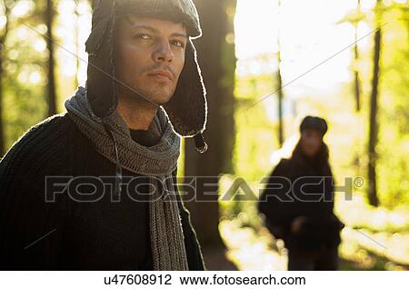 Stock Image - Portrait of mid adult man wearing hat and scarf, woman in background. Fotosearch