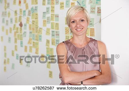 Stock Photo - Portrait of mid adult woman with adhesive notes in background. Fotosearch