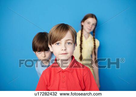 Stock Image - Portrait of three children looking at camera, blue background. Fotosearch