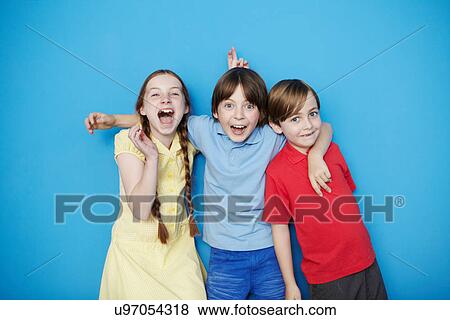 Stock Photo - Portrait of three children with arms around each other against blue background. Fotosearch