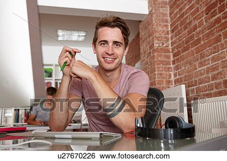 Stock Photograph - Portrait of young man at desk. Fotosearch