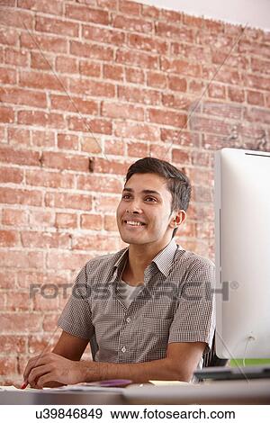 Stock Photo - Portrait of young man at desk with brick wall. Fotosearch