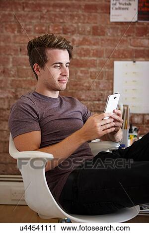 Stock Image - Portrait of young man sitting on chair using digital tablet. Fotosearch