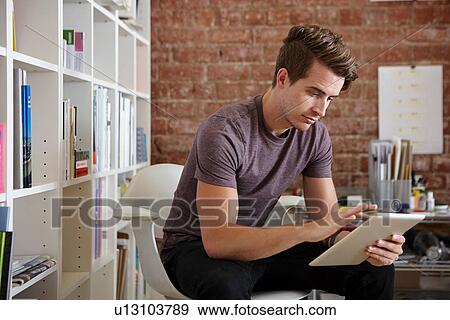 Portrait of young man sitting on chair using digital tablet View Large Photo Image Stock Photo - Portrait of young man sitting on chair using digital tablet. Fotosearch
