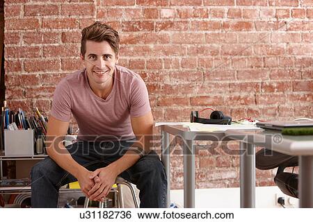 Portrait of young man sitting on chair in creative office View Large Photo Image Stock Photograph - Portrait of young man sitting on chair in creative office. Fotosearch