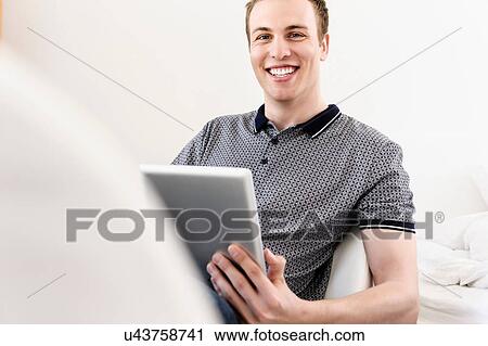 Portrait of young man sitting with digital tablet View Large Photo Image Stock Image - Portrait of young man sitting with digital tablet. Fotosearch