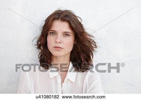 Stock Image - Portrait of young woman against white wall. Fotosearch