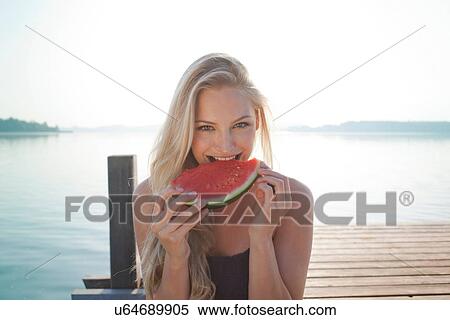 Stock Photography - Portrait of young woman at lake eating watermelon. Fotosearch