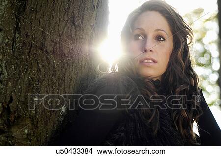 Picture - Portrait of young woman by tree trunk in autumn. Fotosearch