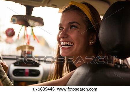 Stock Image - Portrait of young woman in car, smiling. Fotosearch