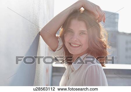 Stock Image - Portrait of young woman leaning against wall. Fotosearch
