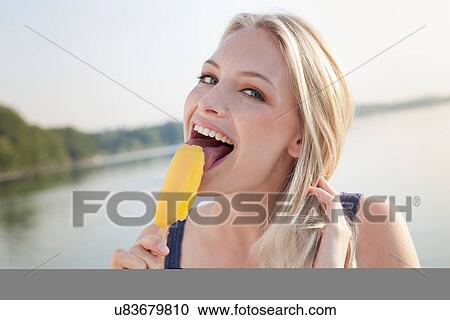 Stock Image - Portrait of young woman licking ice lolly. Fotosearch