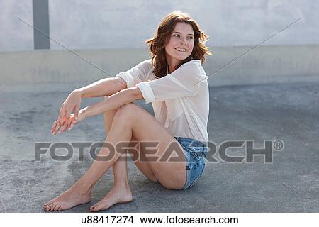 Picture - Portrait of young woman sitting on concrete floor. Fotosearch