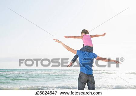 Stock Photo - Rear view of girl sitting on father's shoulders with arms wide. Fotosearch