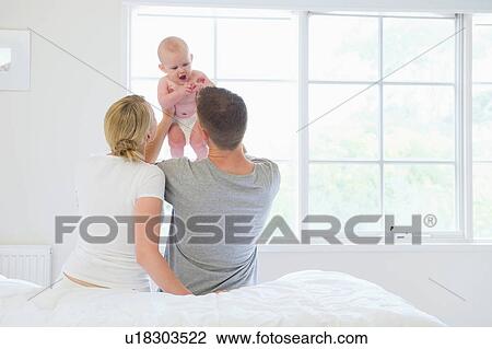 Rear view of parents holding baby View Large Photo Image Stock Image - Rear view of parents holding baby. Fotosearch
